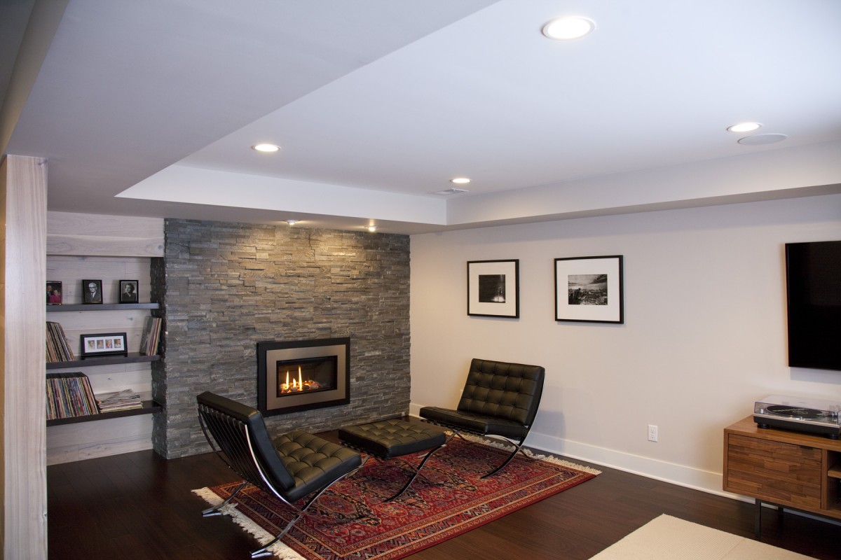 <p>The owners of this home desired to update their 1970s-style basement to fit continuously with the midcentury modern aesthetic of the rest of their home. The popcorn ceiling and old carpet were removed, and restructured duct work created an intentional design for the ceiling. New Peruvian walnut flooring and a new fireplace insert with surrounding stone create a simple, modern look in keeping with the tastes of the homeowners and style of the home. Details like the bar area and hickory wall paneling (actually flooring put on the wall!) provide them with a customized space that is uniquely their own.</p>
