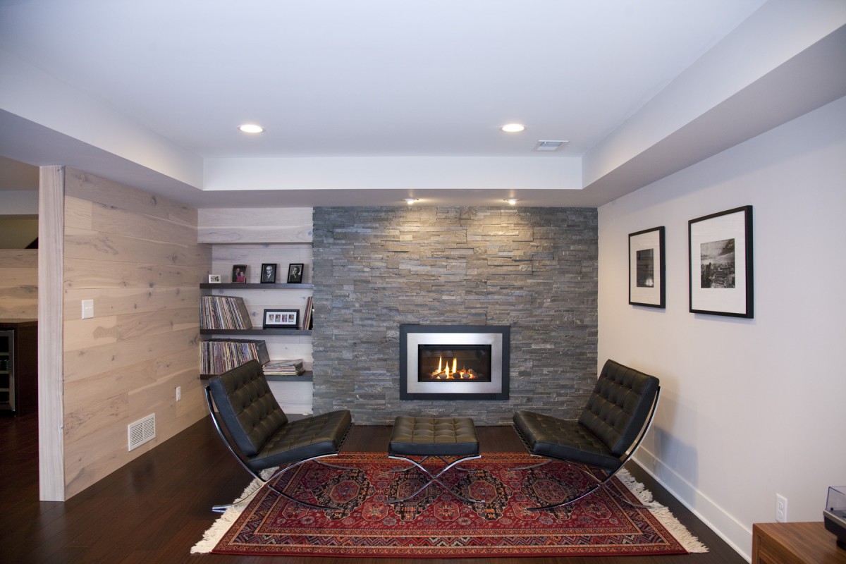 <p>The owners of this home desired to update their 1970s-style basement to fit continuously with the midcentury modern aesthetic of the rest of their home. The popcorn ceiling and old carpet were removed, and restructured duct work created an intentional design for the ceiling. New Peruvian walnut flooring and a new fireplace insert with surrounding stone create a simple, modern look in keeping with the tastes of the homeowners and style of the home. Details like the bar area and hickory wall paneling (actually flooring put on the wall!) provide them with a customized space that is uniquely their own.</p>
