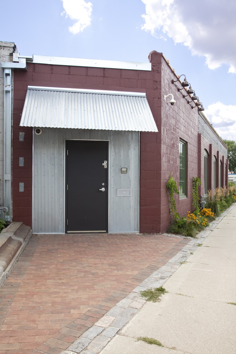 <p>This entrance to the building had been boarded up, and is now welcoming with new lighting, a new patio, and a corrugated steel overhang.</p>
